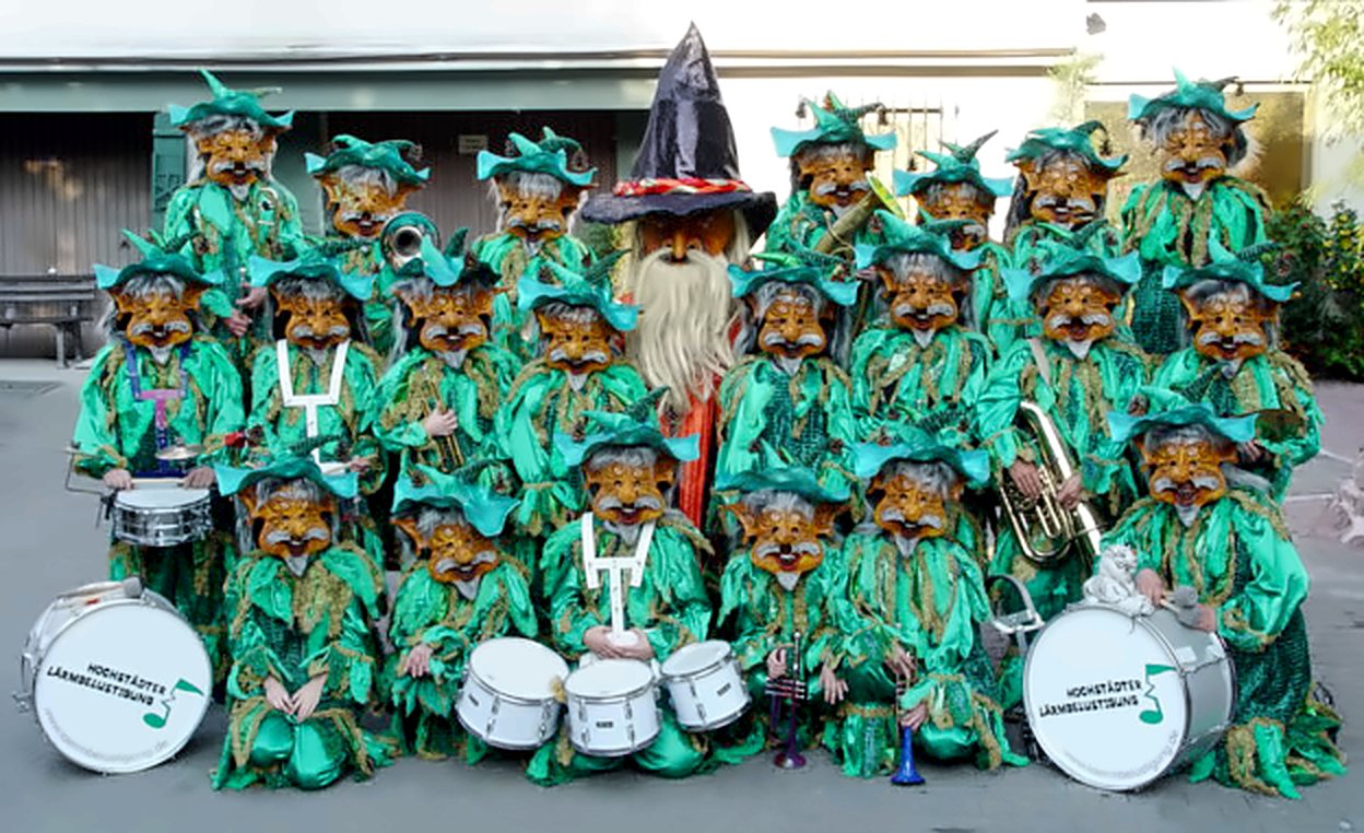 Gruppenfoto der Hochstädter Lärmbelustigung in grünen Kostümen mit Masken, vorne Trommeln mit Lärmer-Logo, in der Mitte eine Figur mit spitzem Hut und langem Bart